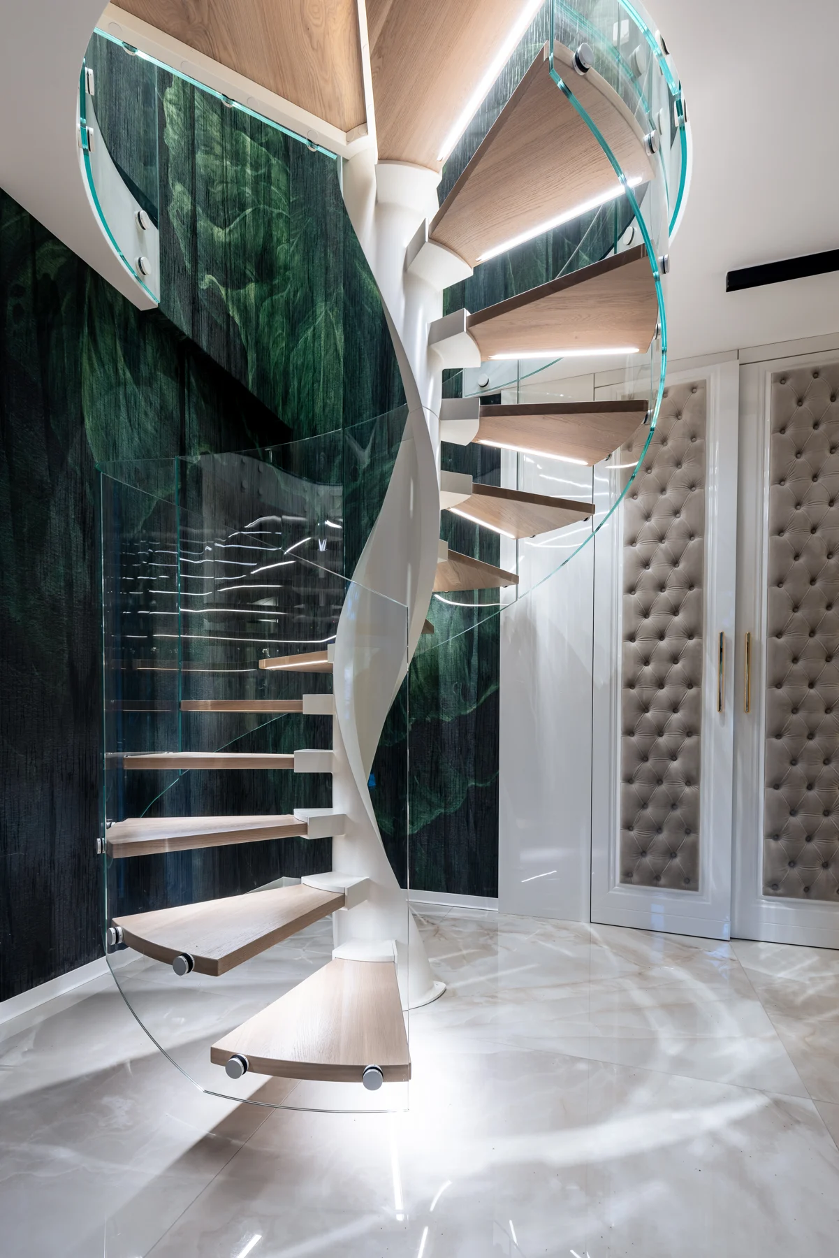 Wendeltreppe mit Holzstufen und Glasgeländer vor einer grünen Wand