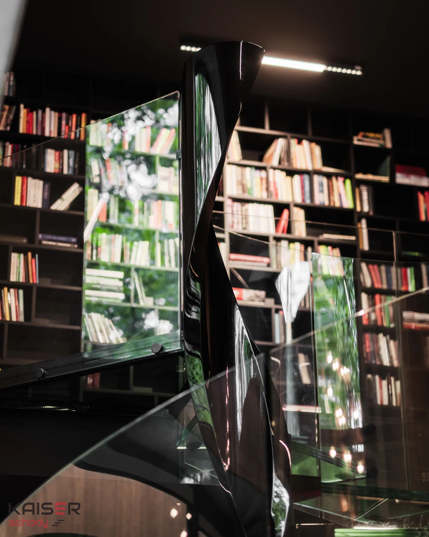 Oberer Treppenaustritt mit Glasbrüstung neben einer Bibliothek